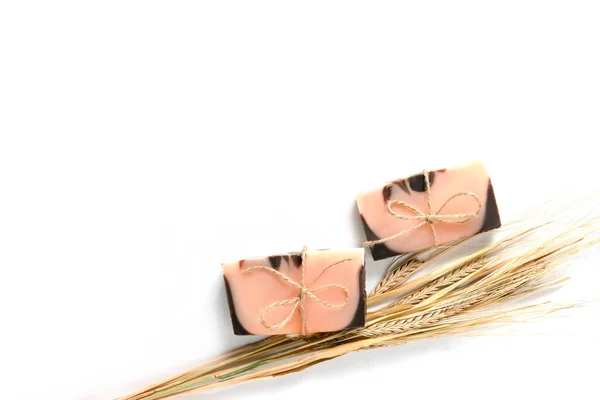 Düz kompozisyon, iki el yapımı kahverengi-pembe sabun ve ahşap desenli beyaz arka planda bir buğday sapı vardı. Yatay fotoğraf, metin için telif uzayı. - Evet. El yapımı kozmetik konsepti