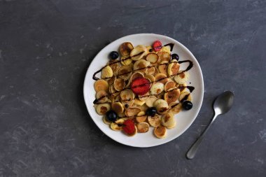 Çikolata, krep lapası ile sulandırılmış küçük bir tabakta küçük krepler kahvaltıda, düz yerde, yaban mersinli ve çilekli küçük gözlemeler