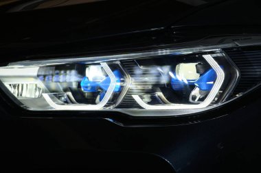 Bir arabanın güzel ve vahşi gözleri. Mavi ksenon ışıkları ve güçlü spor otomobillerinin kaputuyla yırtıcı farlar..