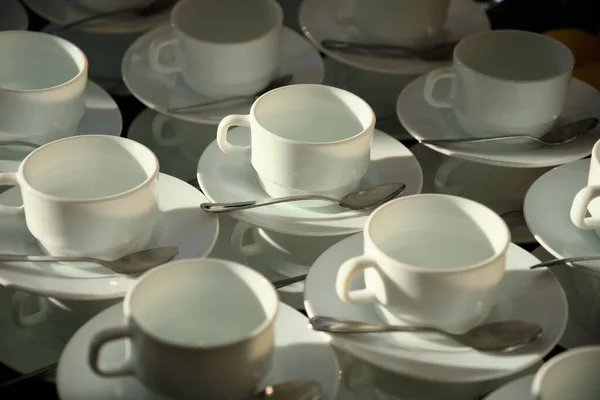 Cups and spoons in a line. Pattern of a group of empty white cups, sausers and spoons for coffee and tea, standing on  table of each other to serve for breakfast or buffet at catering