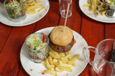 Patates kızartmalı ve yeşil salatalı bir hamburger.