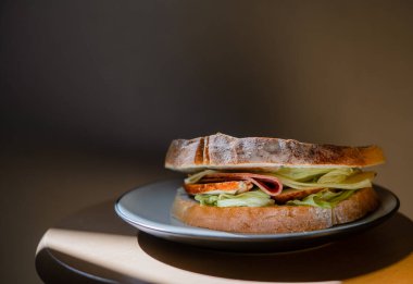 Jambonlu sandviç ve siyah arka planda beyaz tabakta salata.