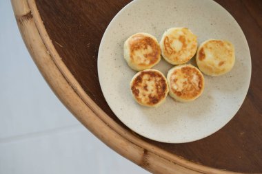 Ahşap bir masada beyaz bir tabakta süzme peynir krepleri.