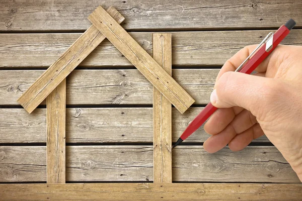 Arquiteto desenhando uma casa de madeira conceitual em fundo de madeira — Fotografia de Stock