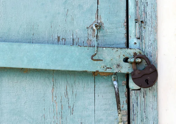 Mavi kapısında metal saplı metalik paslı bir kilit. Kapı eski ve sarılı..