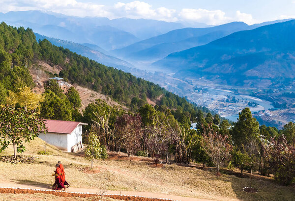 Two Buddhist monks in their traditional red clothes on the territory of women Buddhist Monastery in Bhutan, Punakha valley on the backgroun