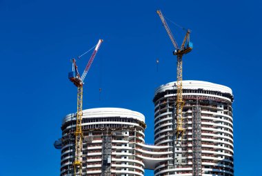 Tel Aviv, İsrail - 29 Temmuz 2019: Parlak mavi gökyüzü ve yüksek bina arka planında modern bir gökdelenin inşasına bağlı iki bina vinci.