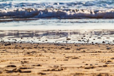 Gün batımında kumsala yakın kum ve deniz dalgası. Güneş sakin sahile yansıyor. Yumuşak odaklanma. Yaz tatili geçmişi.