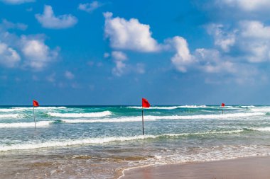 Deniz dalgalarında yüzmek tehlikelidir. Kumsaldaki fırtınalı havada rüzgarda dalgalanan kırmızı uyarı bayrağı..