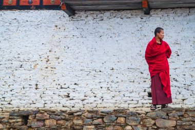 Thimphu / Bhutan - 28 Şubat 2016: Himalaya dağlarındaki manastırda beyaza boyanmış taş duvarın arkasındaki geleneksel kırmızı elbiseli genç Budist rahip..