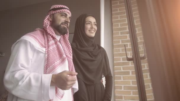 Αραβικό ζευγάρι κοιτάζει από το παράθυρο στο σπίτι. — Αρχείο Βίντεο