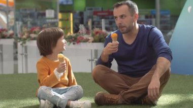 Baba oğul parkta dondurma yiyorlar.