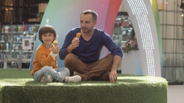 Vader en zoon genieten van ijs buiten in een park — Stockvideo