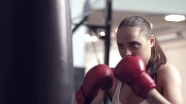 Kadın boksör boks stüdyosunda büyük bir kum torbasına vuruyor. Kadın boksör sıkı çalışıyor..