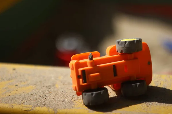 Broken toy tractor without wheel lies on the edge of sandbox on its side