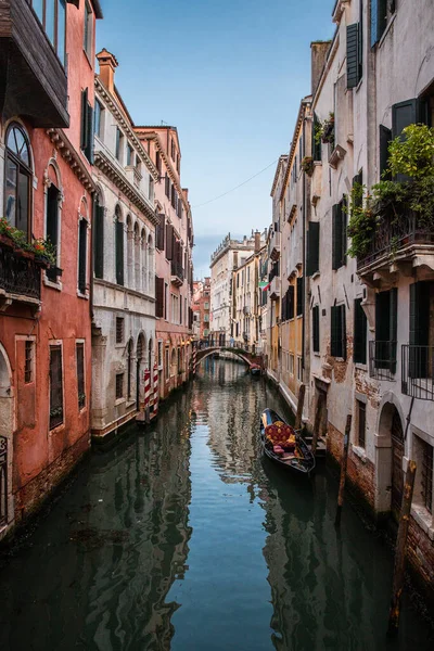 Küçük bir köprü ve pembe turuncu evler Venedik, İtalya 'da günbatımında bir kanala ve geleneksel bir gondola yansıyor. Etrafta kimse yok. Tecrit, karantina.