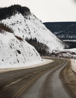 Alaska, Anchorage 'dan Matanuska Buzulu' na giden Palmer yakınlarında kar fırtınası öncesi Glenn Hwy. Kış zamanı. Yan taraflarda kar dağları ve arkada evler. Yol ıslak..