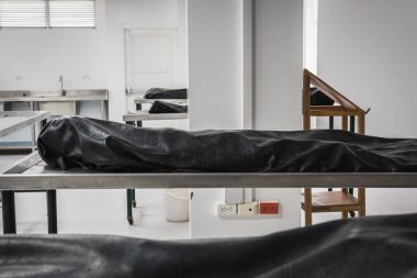 Covered human corpses on tables in a morgue / mortuary waiting for identification, autopsy, burial or cremation. Taken in Armenia, Colombia. The bodies are in a big, lonely room; they are covered with black blankets; might be the victims of pandemic. clipart