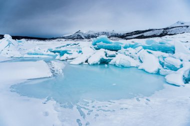 Matanuska Buzulu, Alaska 'da eşsiz buz oluşumları ve mağaralarla çevrili güzel donmuş gölet / tarn. Her yerde kar var ve arkada dağlar yükseliyor. Kışın yapılan bir yürüyüş sırasında çekilmiş..
