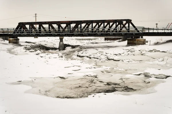 Winter landscape with a bridge & ice breaking, cracking and melting from a frozen creek / river in the north of Anchorage, Alaska. Taken next to Ship Creek Small Boat Launch.