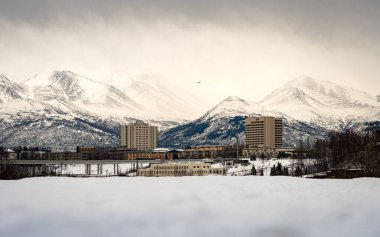 Caddelerin arkasındaki Chugach Park 'ın güzel dağları Anchorage, Alaska' daki evler ve binalar. Port Ship Creek Küçük Teknesi 'nden alınmıştır. Kış boyunca kar ve bulutla kaplıyken.. 