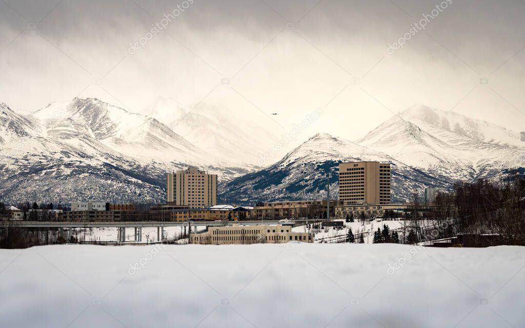 Beautiful mountains of Chugach Park behind the streets, houses & buildings of Anchorage, Alaska. Taken from Port Ship Creek Small Boat Launch during the winter when covered with snow and cloudy. 