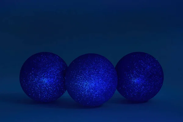 Three glitter christmas balls on dark blue background. Copy space, selective focus