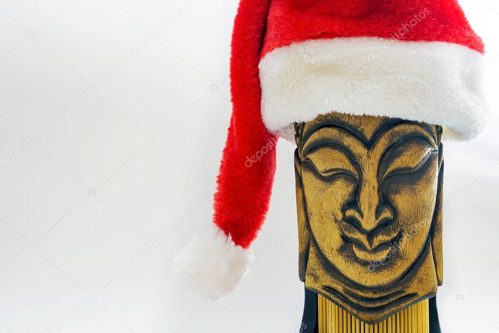 wooden face of buddha in santa claus hat on white background, selective focus, copy space