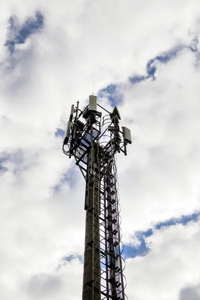 Cellular communications tower on cloudy sky background in daytime
