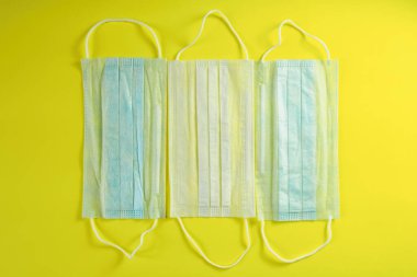 Sarı arka planda tıbbi maskeler. Koronavirüs, alerji, grip ve virüse karşı koruma kavramı. Cerrahi maske, üst manzara.