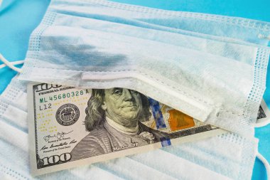 Tıbbi maske ve 100 dolarlık banknot mavi arka planda. Açık kavramı, spekülasyon ve indirimdeki yüz maskesi kıtlığı. Seçici odak, yakın plan