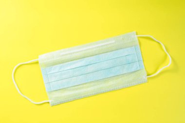 Sarı arka planda tek kullanımlık tıbbi maske. Koronavirüs, alerji ve gribe karşı koruma kavramı. Cerrahi maske, üst manzara.