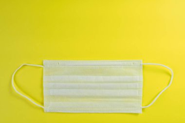 Sarı arka planda beyaz tıbbi maske. Koronavirüse karşı koruma, alerji, grip. Cerrahi maske, üst görünüm, kopyalama alanı