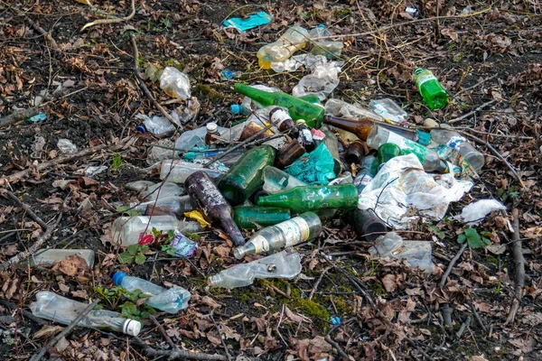 Heap of dirty plastic, glass bottles and other non recycled waste on ground in forest. Environmental pollution.