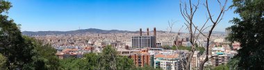 Montjuic tepesinden Barcelona bölgelerine kadar uzanan bir panorama. Önünde ağaçlar var.
