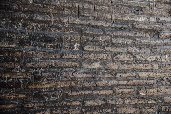 Üzerinde çizikler ve modern etiketler olan antik tuğla bir duvar.