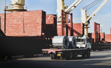 Kamyon, büyük geminin yanına çelik bobinleri yüklüyor. Limandaki bir gemiden çelik kargo boşaltılmış. Malzeme lojistik konsepti.