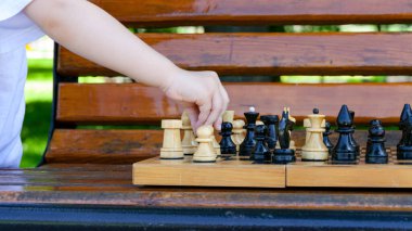 Parktaki bankta bir çocuk satranç tahtasına hamle yapıyor..