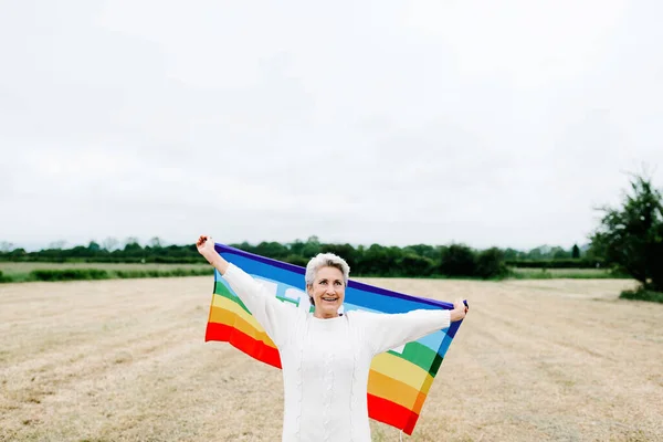 Yaşlı kadın ve lezbiyen. Mutlu, gülümseyen ve kameranın önünde gökkuşağı eşcinsellik bayrağı tutan. LGBT konsepti ve yaşlılık.