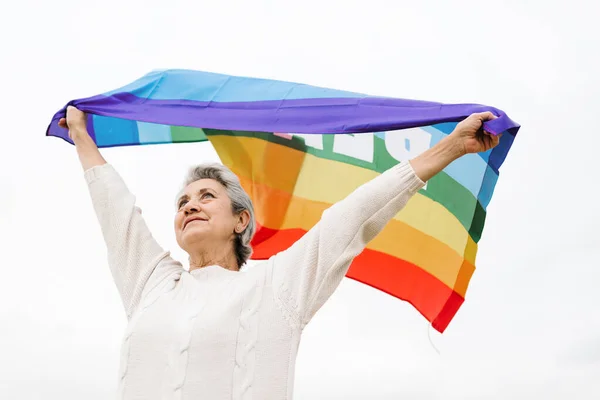 Kafasında LGBT bayrağı sallayan yaşlı bir kadının alçak açılı görüntüsü. LGBT konsepti ve yaşlılık. beyaz arkaplan
