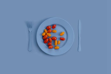 Mavi tabakta kırmızı ve sarı domatesler, mavi bıçak, mavi çatal, mavi arka planda. Yukarıdan manzara. Reklam ve pazarlama iletişiminin yanı sıra gıda ve gıda ürünlerinin tasarımı için yaratıcı bir fikir olarak uygun.
