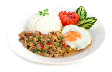 Tayland yemekleri kızarmış domuz baharatı ve fesleğenli pilav ve kızarmış yumurta ve domates salatalığı ile servis edilmiş beyaz arka plana oyulmuş beyaz tabak.