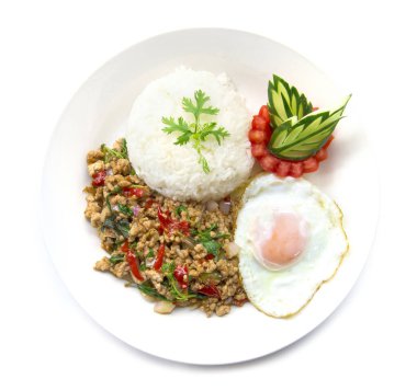 Tayland yemekleri kızarmış domuz baharatı ve fesleğenli pilav ve kızarmış yumurta ve domates salatalığı ile servis edilmiş beyaz arka planda izole edilmiş beyaz tabak.