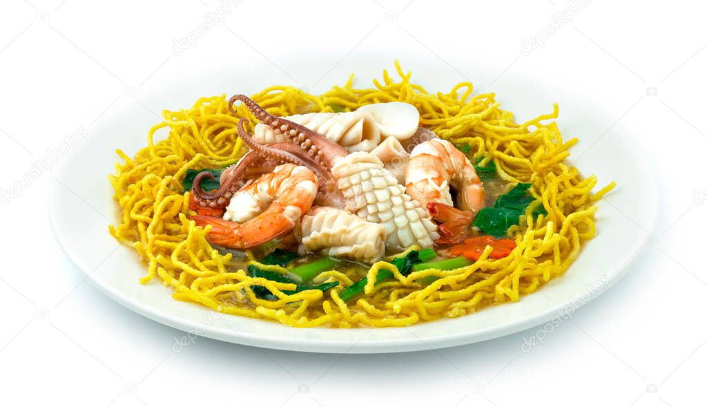 Crispy Egg Noodles with Seafood,Shrimps, Squid and Kale soaked in Gravy Soy Sauce on white Plate. Chinese Food Asian style Decorate carved carrots flower shape sideview