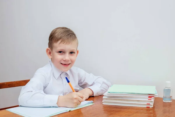 Мальчик сидит за столом, держа в руках ручку, рядом тетради и учебники — стоковое фото