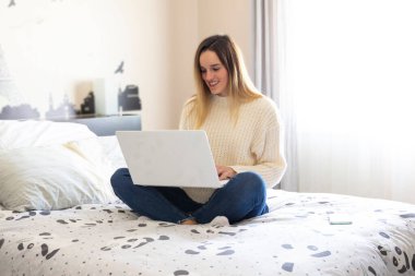 Evinden gülümseyerek yatakta telgraf çeken bir kadının fotoğrafı. Coronavirus karantinası. Uzaktan çalışan kadın..