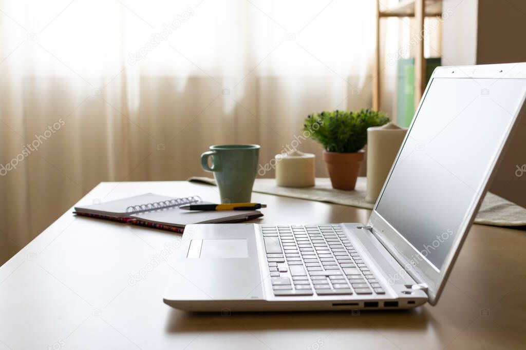 Picture of a welcoming environment of a home office desk with laptop, papers and a cup of coffee and some candles in the background. Telecommuting vibes.