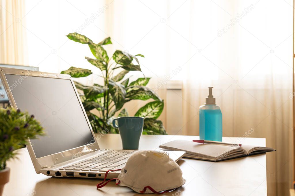 Photography of a home office with a laptop on the desk and some medical ppe while teleworking.