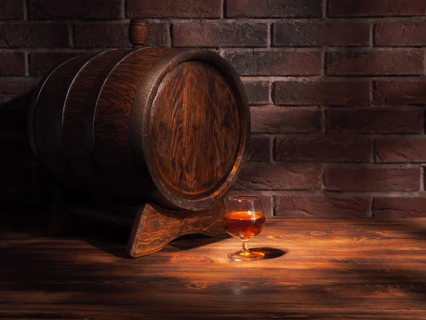 Glass of cognac with barrel on wooden table — Stock Photo, Image