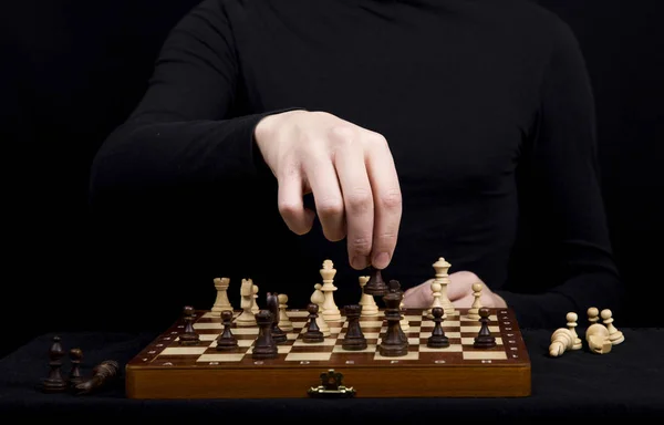 Man in een zwarte jas transponeert een pion op een houten schaakbord — Stockfoto